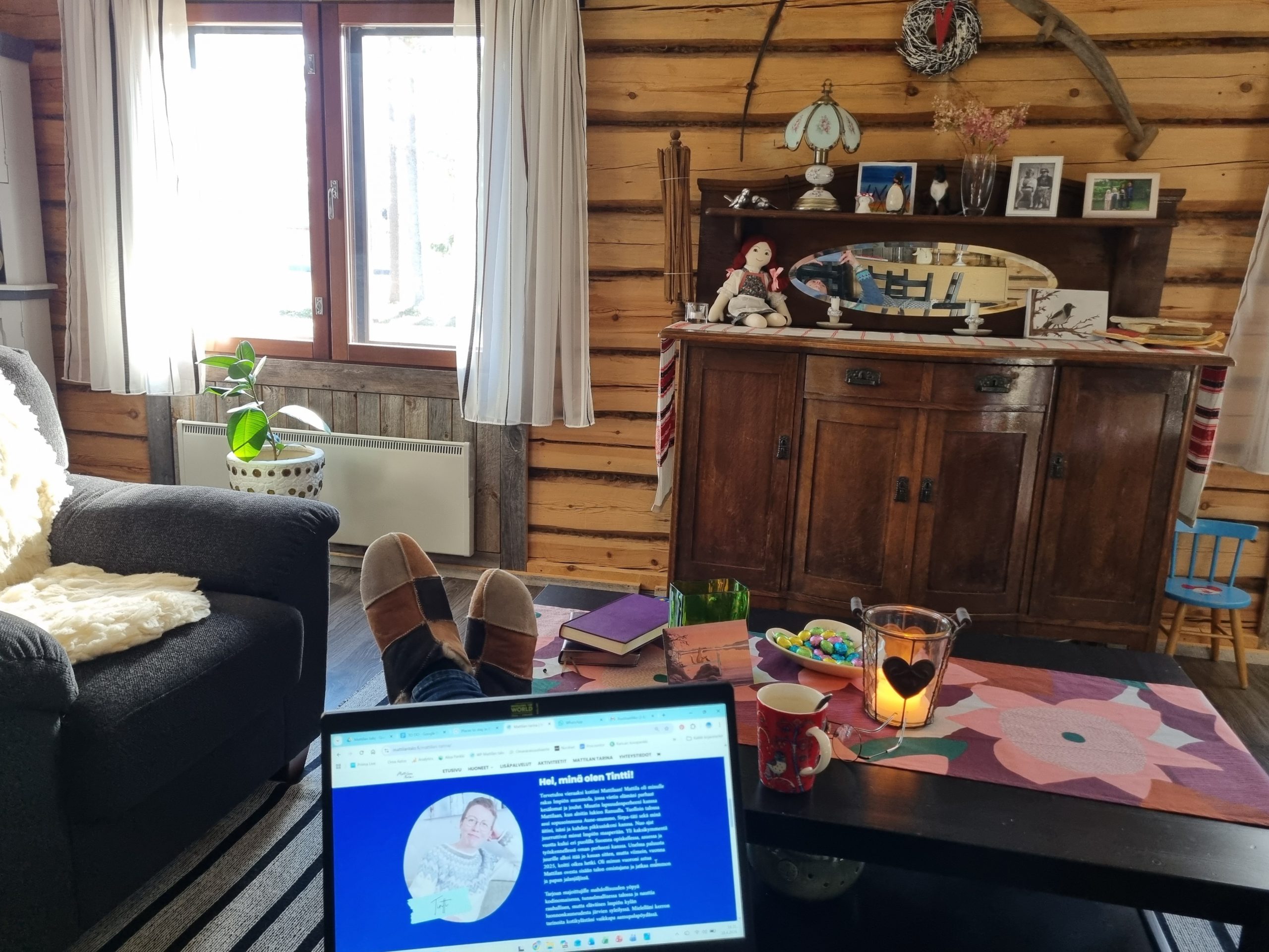 hirsiseinäinen pirtti, jalat pöydällä ja tietokone sylissä